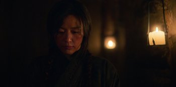 Movie still from “Kingdom: Ashin of the North” (2021), directed by Kim Seong-hun – A woman in a dark room with a candle in the background; Close Up shot, Over the shoulder angle