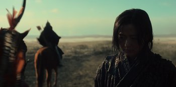 Movie still from “Kingdom: Ashin of the North” (2021), directed by Kim Seong-hun – A woman standing on a dirt field next to a horse; Close Up shot, Low angle