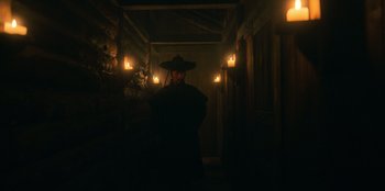 Movie still from “Kingdom: Ashin of the North” (2021), directed by Kim Seong-hun – A man wearing a hat standing in a dark room; Wide shot, Low angle