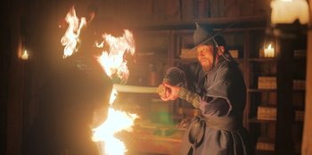 Movie still from “Kingdom: Ashin of the North” (2021), directed by Kim Seong-hun – A man holding a sword in front of a fire pit; Medium shot, Low angle