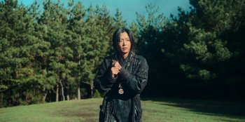 Movie still from “Kingdom: Ashin of the North” (2021), directed by Kim Seong-hun – A person standing in a field with trees in the background; Medium shot, Low angle