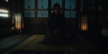Movie still from “Kingdom: Ashin of the North” (2021), directed by Kim Seong-hun – A person sitting on the ground in a dark room; Wide shot, High angle