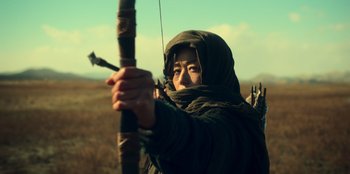 Movie still from “Kingdom: Ashin of the North” (2021), directed by Kim Seong-hun – A person holding a bow and arrow on a field; Medium shot, Low angle