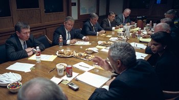 Movie still from “Kingdom of Silence” (2020), directed by Rick Rowley – A group of people sitting at a table eating food; Medium shot, High angle