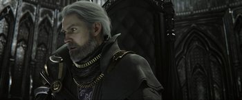 Movie still from “Kingsglaive: Final Fantasy XV” (2016), directed by Takeshi Nozue – A man with a beard wearing a black jacket and a gold necklace; Close Up shot, Over the shoulder angle