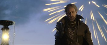 Movie still from “Kingsglaive: Final Fantasy XV” (2016), directed by Takeshi Nozue – A man with long hair and a beard standing in front of a bunch of lights; Medium shot, Low angle