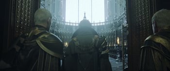 Movie still from “Kingsglaive: Final Fantasy XV” (2016), directed by Takeshi Nozue – Two people in a large room with a statue in the background; Medium shot, Low angle