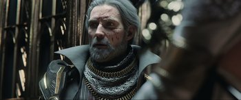 Movie still from “Kingsglaive: Final Fantasy XV” (2016), directed by Takeshi Nozue – An old man with a gray beard wearing chains; Close Up shot, Over the shoulder angle