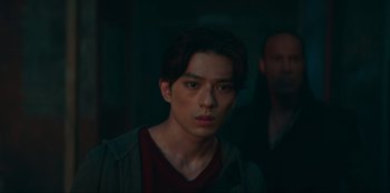 Movie still from “Knights of the Zodiac” (2023), directed by Tomasz Baginski – A young man is looking at the camera while standing next to another man; Close Up shot, Low angle