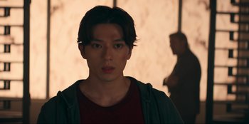 Movie still from “Knights of the Zodiac” (2023), directed by Tomasz Baginski – A young man in a red shirt is looking at the camera; Close Up shot, Low angle