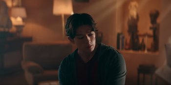 Movie still from “Knights of the Zodiac” (2023), directed by Tomasz Baginski – A man sitting in a living room looking down at the floor; Medium shot, Over the shoulder angle