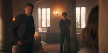 Movie still from “Knights of the Zodiac” (2023), directed by Tomasz Baginski – Two people standing in a room with a lamp on; Medium shot, Over the shoulder angle