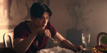 Movie still from “Knights of the Zodiac” (2023), directed by Tomasz Baginski – A man sitting at a table holding a spoon in his hand; Medium shot, Over the shoulder angle