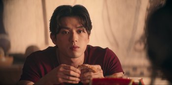 Movie still from “Knights of the Zodiac” (2023), directed by Tomasz Baginski – A man sitting at a table with a sandwich in front of him; Close Up shot, Low angle