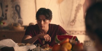 Movie still from “Knights of the Zodiac” (2023), directed by Tomasz Baginski – A man sitting at a table with a knife in his hand; Medium shot, Over the shoulder angle