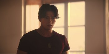 Movie still from “Knights of the Zodiac” (2023), directed by Tomasz Baginski – A man with a necklace standing in front of a window; Medium shot, Low angle