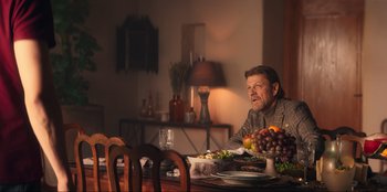 Movie still from “Knights of the Zodiac” (2023), directed by Tomasz Baginski – An older man sitting at a table with a plate of food; Medium shot, Over the shoulder angle