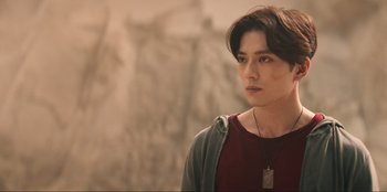 Movie still from “Knights of the Zodiac” (2023), directed by Tomasz Baginski – A young man with long dark hair wearing a red shirt; Close Up shot, Over the shoulder angle