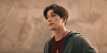 Movie still from “Knights of the Zodiac” (2023), directed by Tomasz Baginski – A young man with long brown hair wearing a red shirt; Close Up shot, Over the shoulder angle