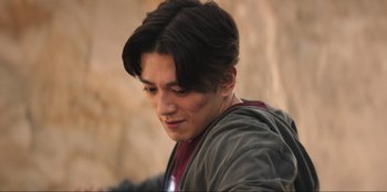 Movie still from “Knights of the Zodiac” (2023), directed by Tomasz Baginski – A young man with long dark brown hair; Close Up shot, Over the shoulder angle