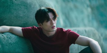 Movie still from “Knights of the Zodiac” (2023), directed by Tomasz Baginski – A young man in a red shirt leaning against a wall; Medium shot, Low angle