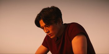 Movie still from “Knights of the Zodiac” (2023), directed by Tomasz Baginski – A man with long dark hair wearing a red shirt; Medium shot, Low angle