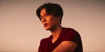 Movie still from “Knights of the Zodiac” (2023), directed by Tomasz Baginski – A young man with short brown hair wearing a red shirt; Close Up shot, Low angle