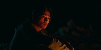 Movie still from “Knights of the Zodiac” (2023), directed by Tomasz Baginski – A man sitting in the dark with his head turned to the side; Close Up shot, Low angle