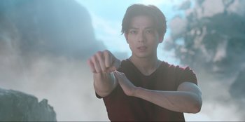 Movie still from “Knights of the Zodiac” (2023), directed by Tomasz Baginski – A young man is holding his hand out to the camera; Medium shot, Low angle