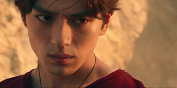 Movie still from “Knights of the Zodiac” (2023), directed by Tomasz Baginski – A young man's face in a red shirt; Close Up shot, Low angle
