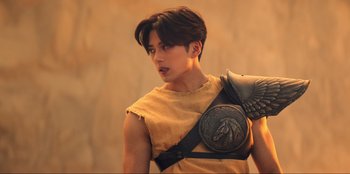 Movie still from “Knights of the Zodiac” (2023), directed by Tomasz Baginski – A young man in a yellow shirt with a shoulder armor; Medium shot, Low angle