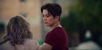 Movie still from “Knights of the Zodiac” (2023), directed by Tomasz Baginski – A young man with dark brown hair and a red shirt; Close Up shot, Over the shoulder angle