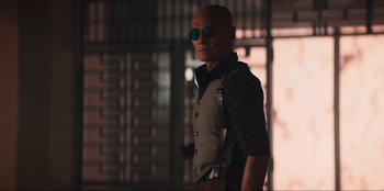 Movie still from “Knights of the Zodiac” (2023), directed by Tomasz Baginski – A man in a vest and sunglasses is standing; Medium shot, Low angle