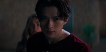Movie still from “Knights of the Zodiac” (2023), directed by Tomasz Baginski – A young man with long dark hair wearing a red shirt; Close Up shot, Low angle