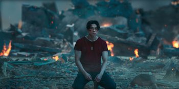 Movie still from “Knights of the Zodiac” (2023), directed by Tomasz Baginski – A man in a red shirt is kneeling in front of fire; Medium shot, Low angle