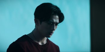 Movie still from “Knights of the Zodiac” (2023), directed by Tomasz Baginski – A young man with long dark hair wearing a red shirt; Close Up shot, Low angle