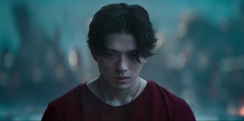 Movie still from “Knights of the Zodiac” (2023), directed by Tomasz Baginski – A young man with long black hair wearing a red shirt; Close Up shot, Low angle