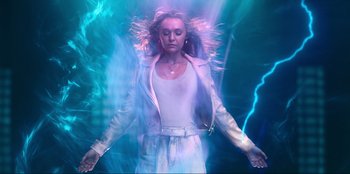 Movie still from “Knights of the Zodiac” (2023), directed by Tomasz Baginski – A woman in a white jacket is standing in front of a blue background; Medium shot, Overhead angle