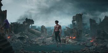 Movie still from “Knights of the Zodiac” (2023), directed by Tomasz Baginski – A shirtless man standing in the middle of a destroyed city; Wide shot, Low angle