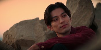 Movie still from “Knights of the Zodiac” (2023), directed by Tomasz Baginski – A man with long dark hair wearing a red shirt; Close Up shot, Low angle