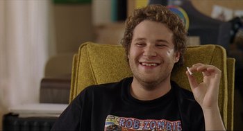 Movie still from “Knocked Up” (2007), directed by Judd Apatow – A man sitting in a chair smiling for the camera; Close Up shot, Overhead angle