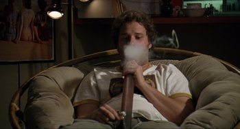 Movie still from “Knocked Up” (2007), directed by Judd Apatow – A man sitting on a couch smoking a pipe; Medium shot, Overhead angle