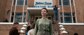 Movie still from “Knowing” (2009), directed by Alex Proyas – A woman standing in front of a building with people in front of it; Medium shot, Low angle