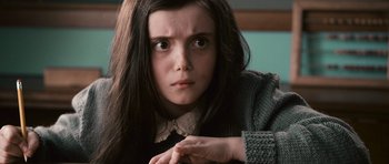 Movie still from “Knowing” (2009), directed by Alex Proyas – A young girl with long dark hair looking at the camera; Close Up shot, Over the shoulder angle