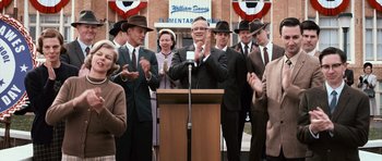 Movie still from “Knowing” (2009), directed by Alex Proyas – A man standing at a podium in front of a group of people; Medium shot, Low angle