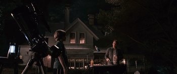 Movie still from “Knowing” (2009), directed by Alex Proyas – A man and a boy standing in front of an outdoor grill at night; Wide shot, Over the shoulder angle