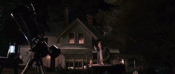 Movie still from “Knowing” (2009), directed by Alex Proyas – A man standing in front of a microphone in front of a house at night; Wide shot, Low angle
