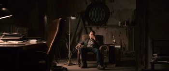 Movie still from “Knowing” (2009), directed by Alex Proyas – A man sitting in a chair in a dark room; Wide shot, Low angle