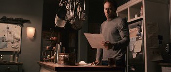 Movie still from “Knowing” (2009), directed by Alex Proyas – A man standing in a kitchen reading a paper; Medium shot, Low angle