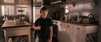 Movie still from “Knowing” (2009), directed by Alex Proyas – A young boy standing in a kitchen holding a backpack; Medium shot, High angle